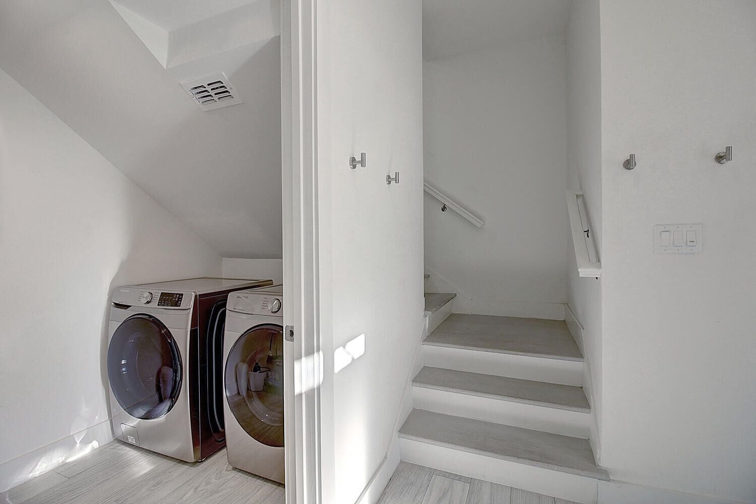 Una sala de bugaderia amb dues rentadores i una escala que porta a un nivell superior.