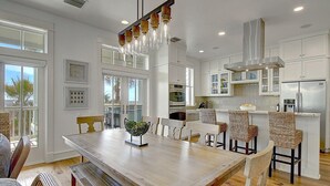 A modern kitchen with white cabinets, stainless steel appliances, and a dining area with a wooden table and wicker chairs. - Sippin' on Sunshine 164 BE (Port Aransas)