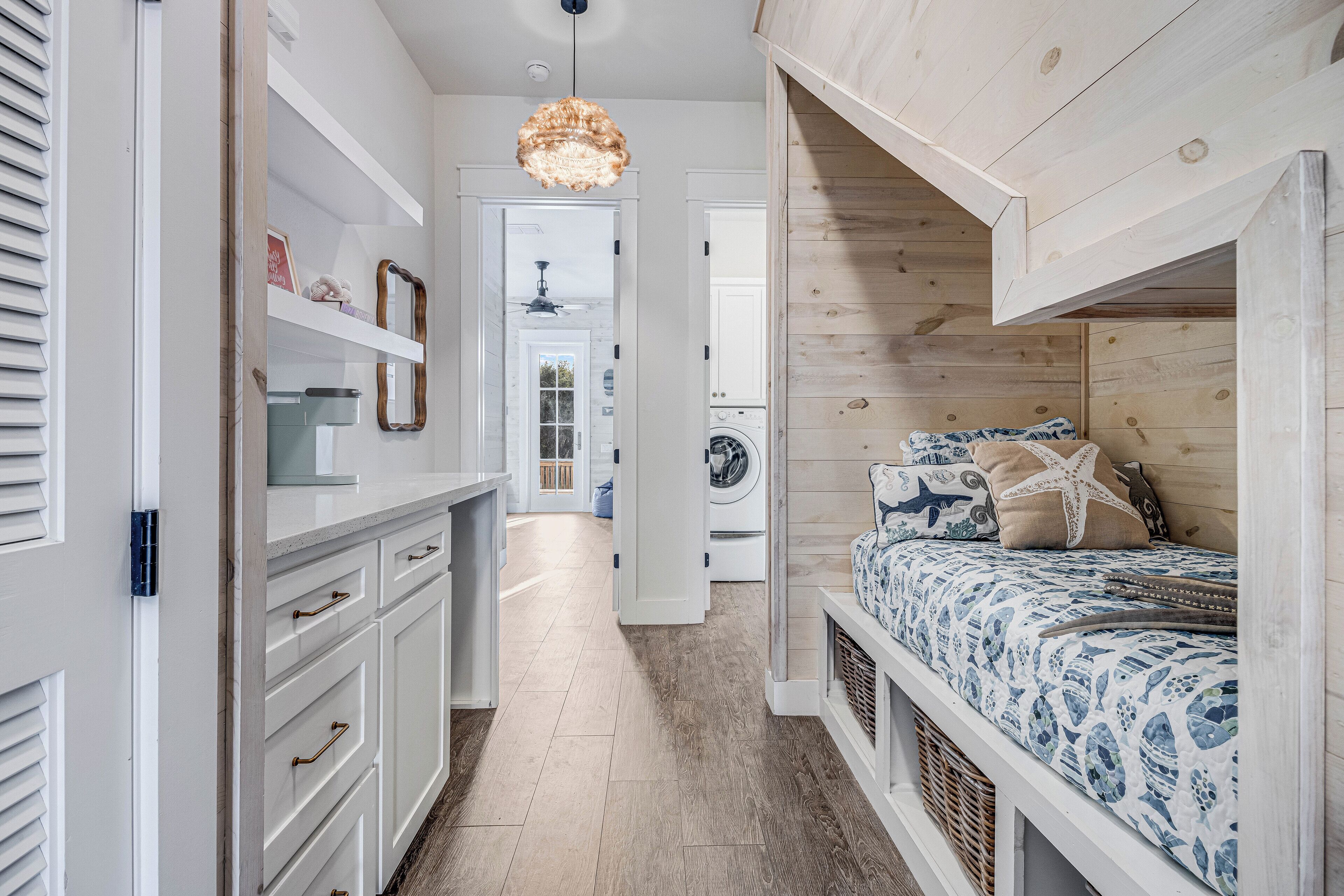 A narrow hallway leading to a bedroom with a bed, a washing machine, and a ceiling fan.