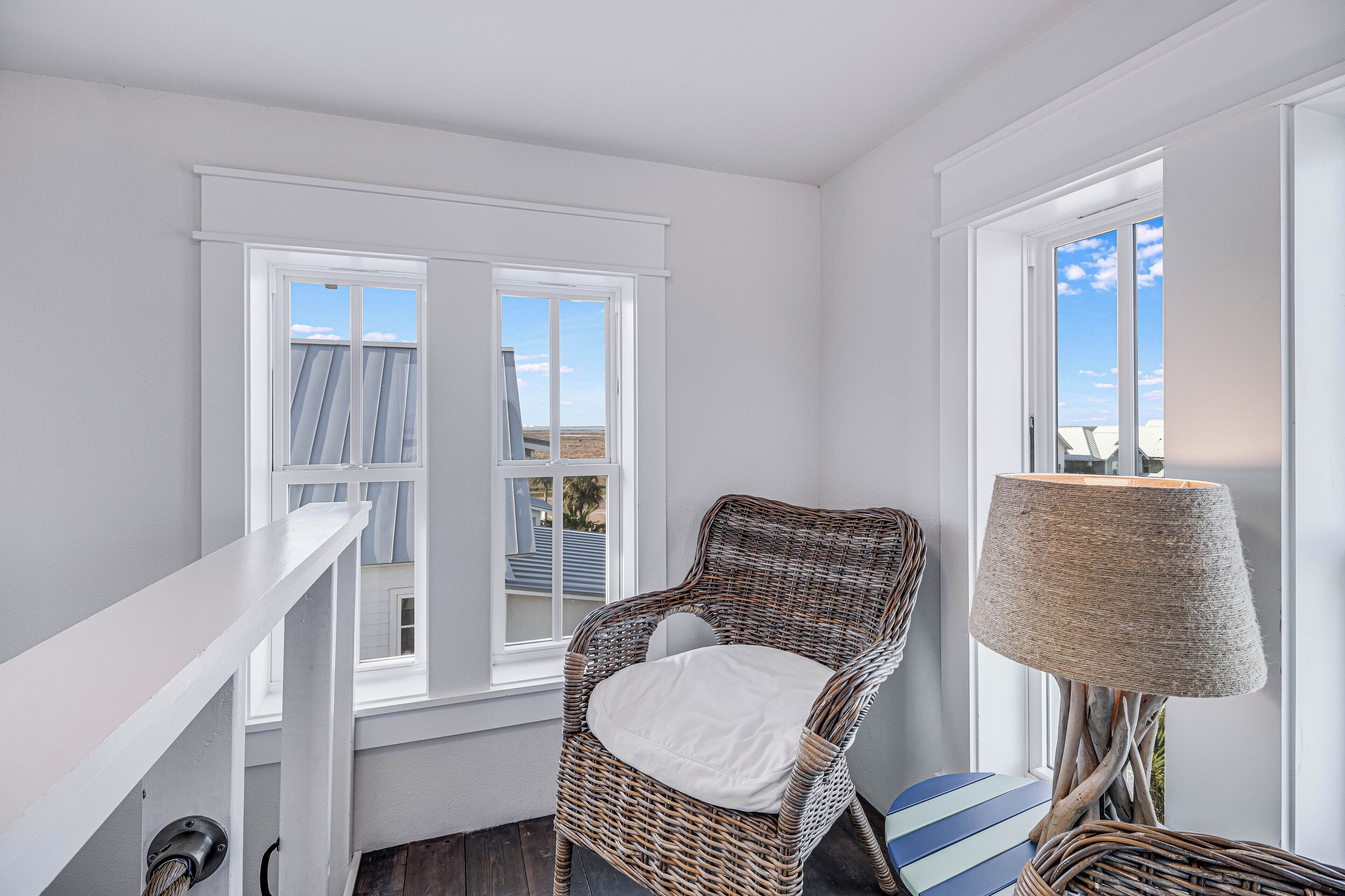 A room with a wicker chair, a lamp, and a view of the sky through a window.