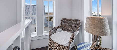 A room with a wicker chair, a lamp, and a view of the sky through a window.