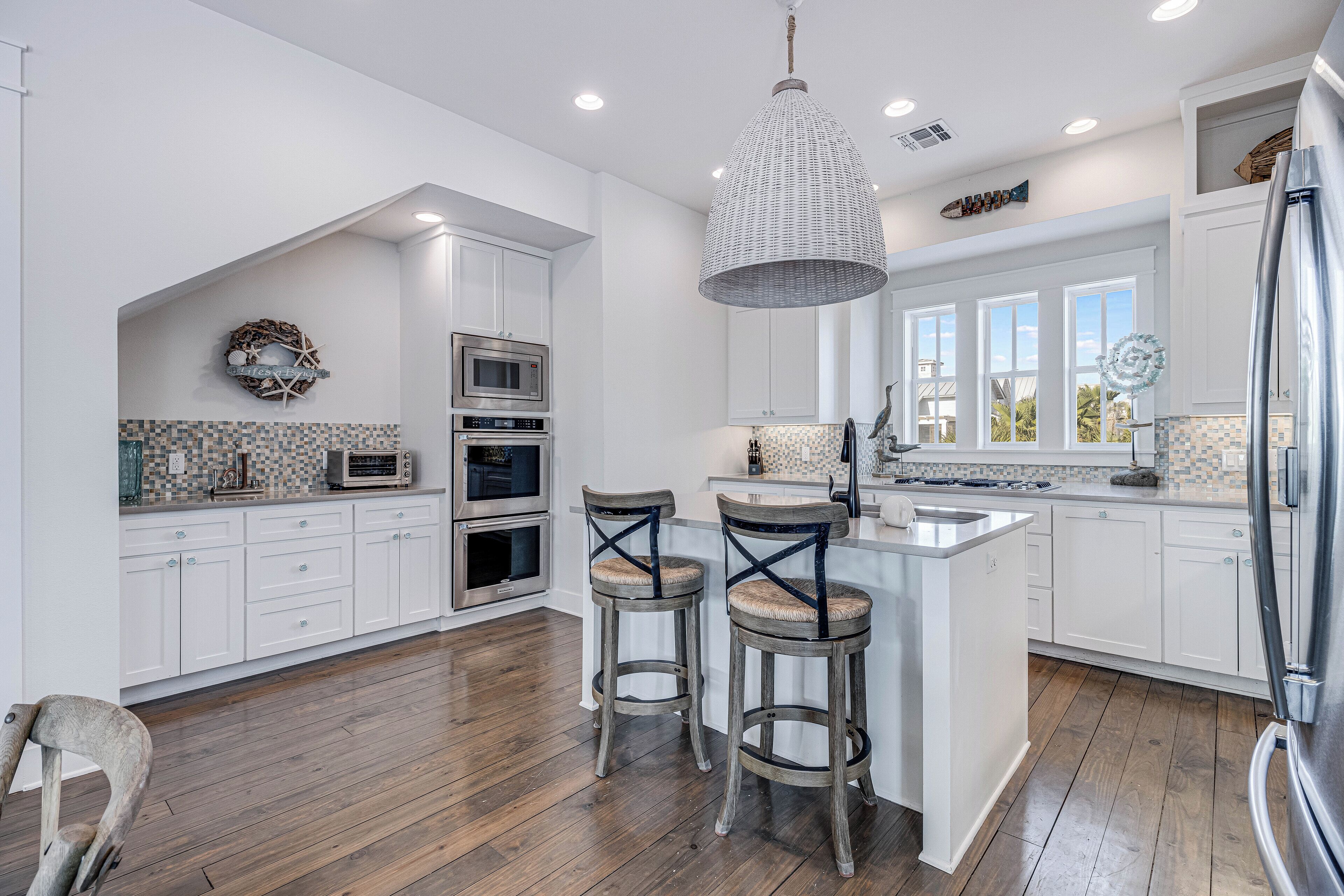 A modern kitchen with white cabinets, a central island, two bar stools, and a hanging light fixture.