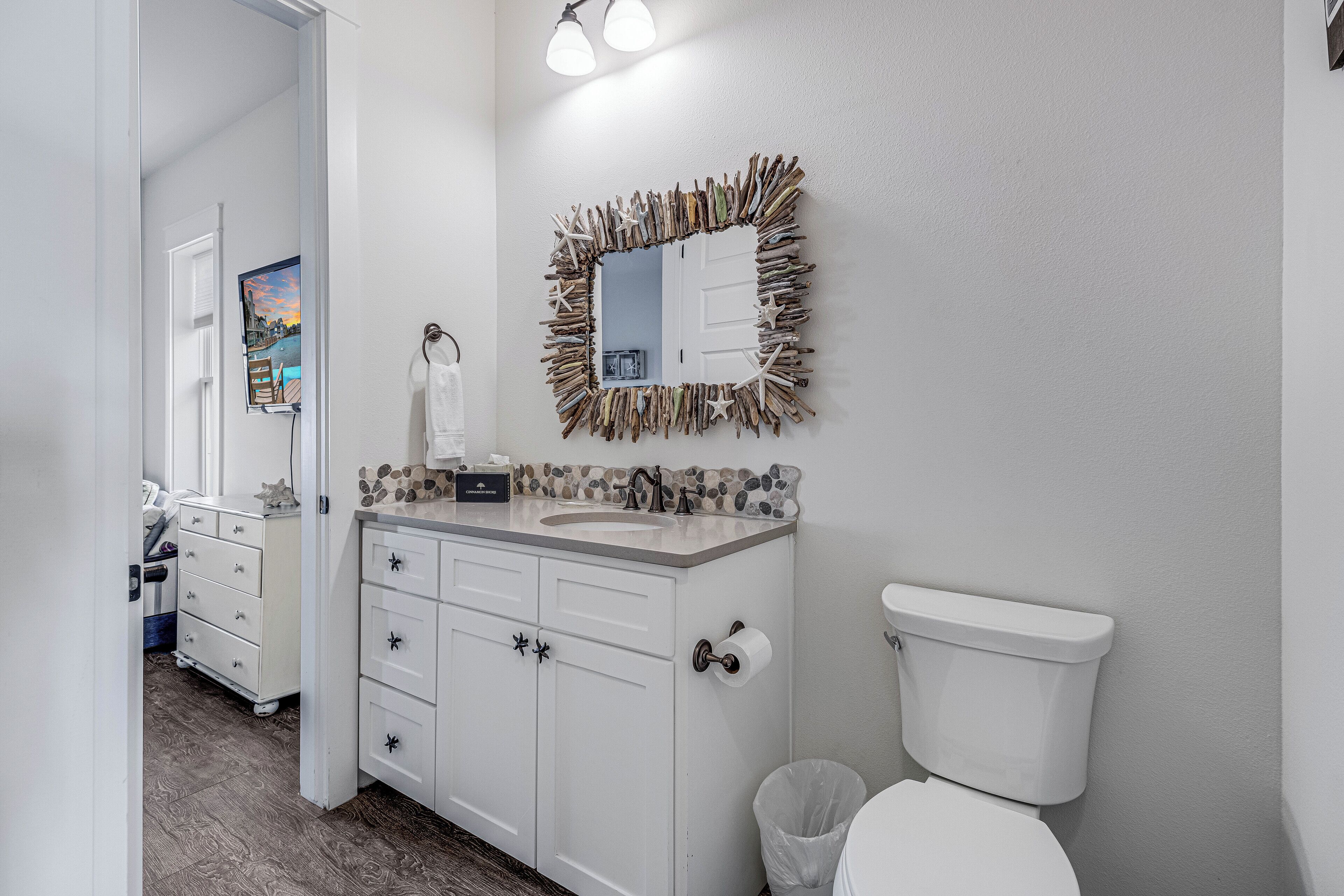 A bathroom with a white vanity, a toilet, and a mirror with a natural frame.