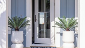 A modern house entrance with a white door, two potted plants, and a wooden deck. - Sand In My Boots 303 HI (Port Aransas)