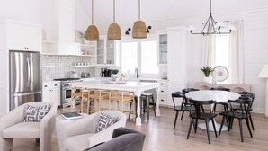 A modern kitchen with white cabinetry, a central island, and a dining area with a round table and chairs. - Sand In My Boots 303 HI (Port Aransas)