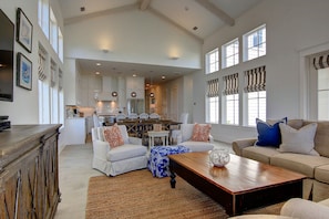 Relax in this spacious living area with a high ceiling, featuring a central coffee table, sofas, and dining area.