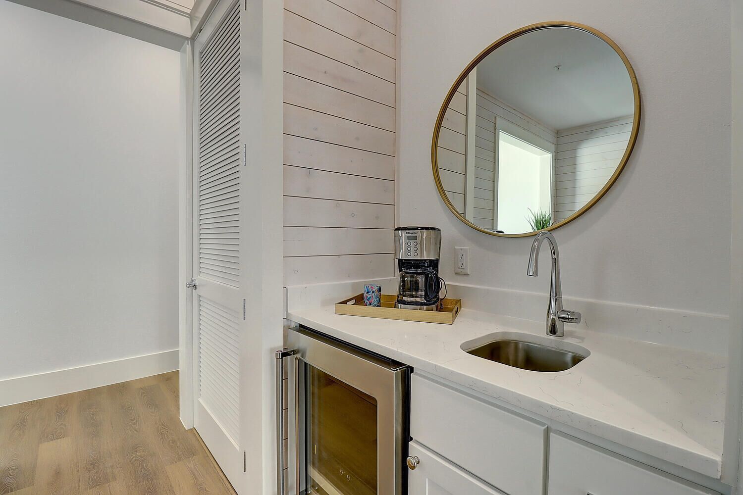 Un bagno compatto con un mobile lavabo bianco, uno specchio rotondo con cornice dorata, una macchina da caffè e un lavandino in acciaio inossidabile.