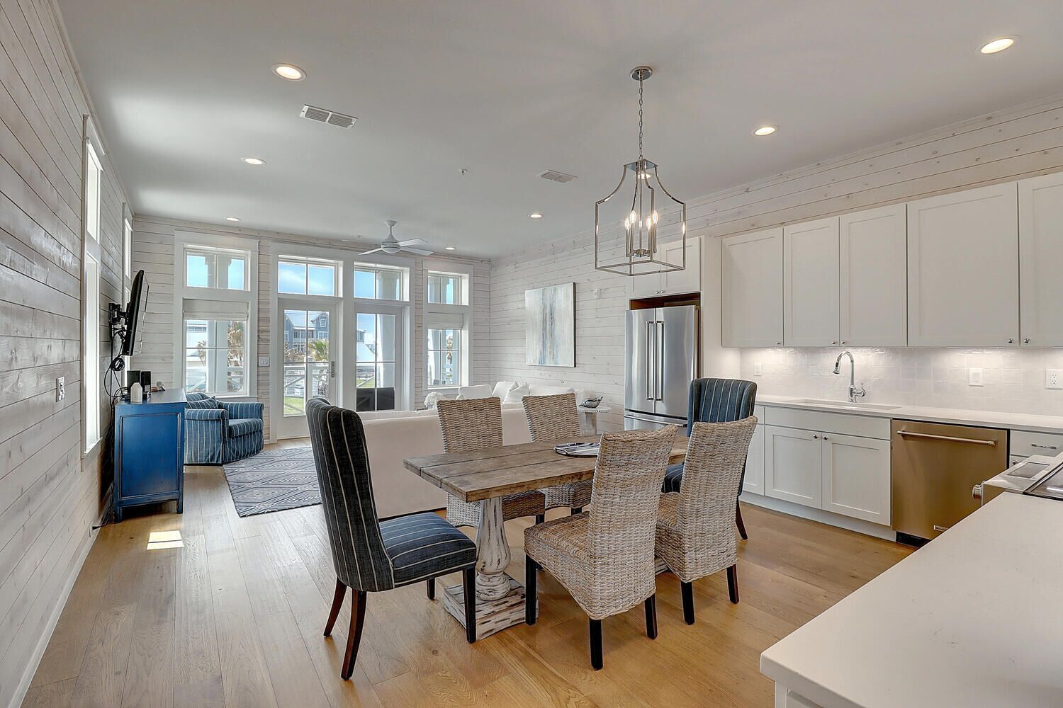 A modern kitchen with white cabinetry, a central island, and a dining area with wicker chairs.