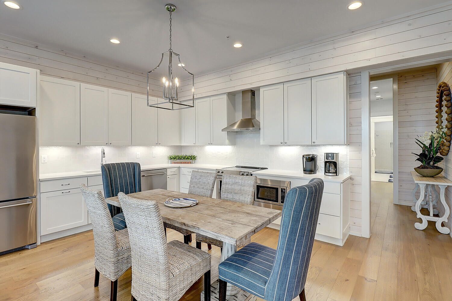 A modern kitchen with white cabinetry, a wooden dining table, and blue-striped chairs.