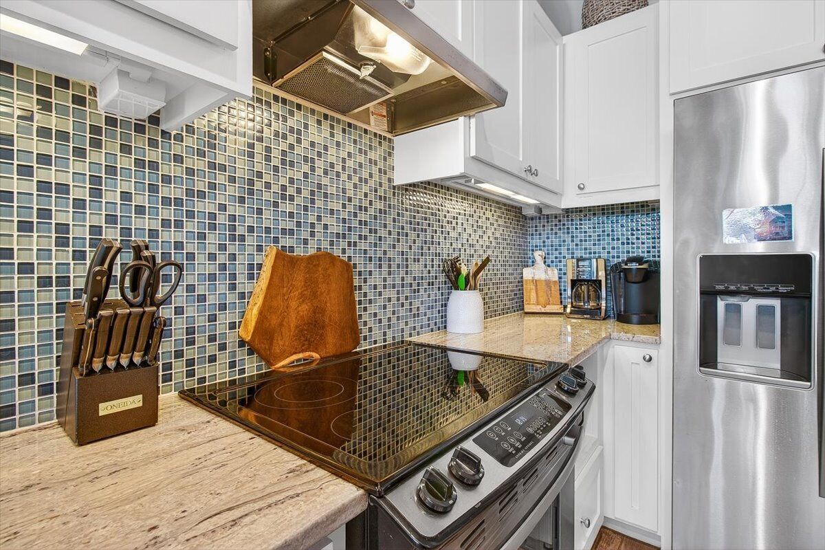A modern kitchen with a glass stovetop, stainless steel appliances, and a backsplash of blue mosaic tiles.