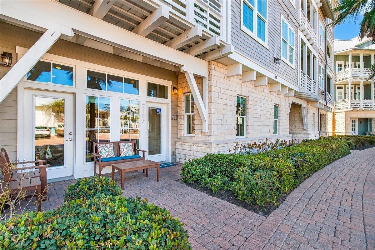 A building with a covered patio area, stone facade, and a small seating area with a bench and chairs.