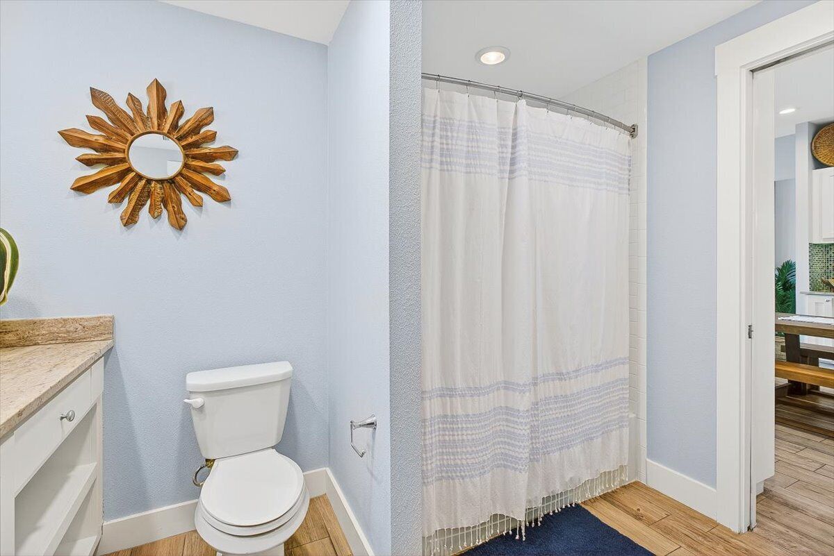 A bathroom with a white toilet, a wooden vanity, a sunburst mirror, and a shower curtain.