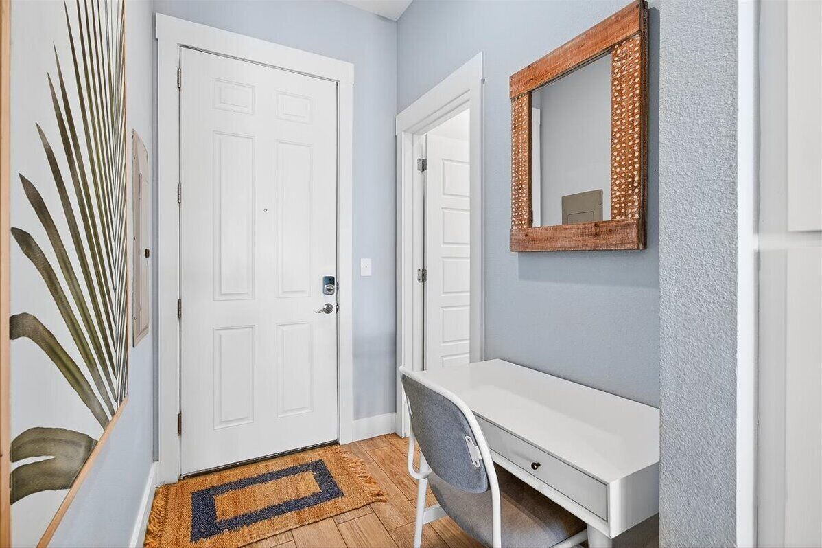 Un couloir avec une porte blanche, un bureau avec une chaise et un miroir accroché au mur.