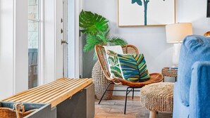 Een gezellige kamer met een rieten stoel, een bank, een grote plant en een kunstwerk in een lijst aan de muur.