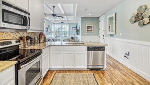 A modern kitchen with white cabinetry, stainless steel appliances, a granite countertop, and a central island. - Turtle Cove TC 1209 (Port Aransas)