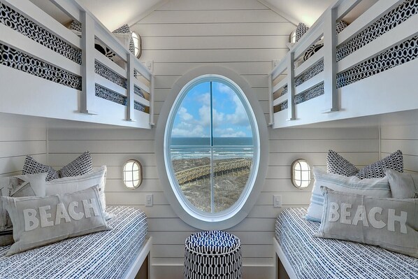 A bedroom with bunk beds, a large round window, and a view of the beach. - The Lighthouse 328 COA (Port Aransas)