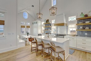 A spacious kitchen with a large island, white cabinetry, and a view of the ocean. - The Lighthouse 328 COA (Port Aransas)