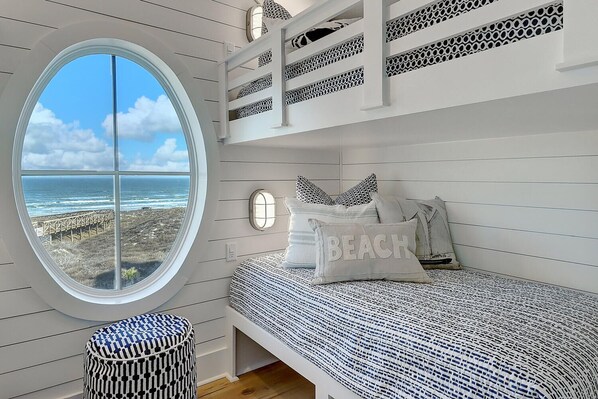 Un dormitorio con un amplio ventanal circular con vistas al océano, una litera y un pequeño otoman redondos.