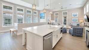 A spacious kitchen with a large island, pendant lighting, and a view of the outdoors through large windows.