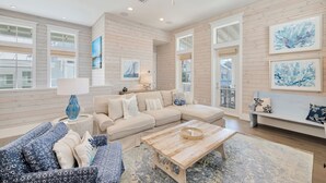 A spacious living room with a large beige sectional sofa, a blue patterned sofa, a wooden coffee table, and a large window with a view of the outside.