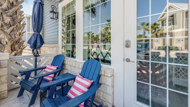A covered patio area with two Adirondack chairs, a blue umbrella, and a stone wall. - The Hideout TC 10101 (Port Aransas)