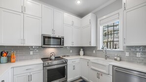 A modern kitchen with white cabinets, a stainless steel microwave, and an oven. - The Hideout TC 10101 (Port Aransas)