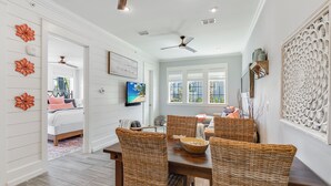 A dining area with wicker chairs, a wooden table, and a television mounted on the wall. - The Hideout TC 10101 (Port Aransas)