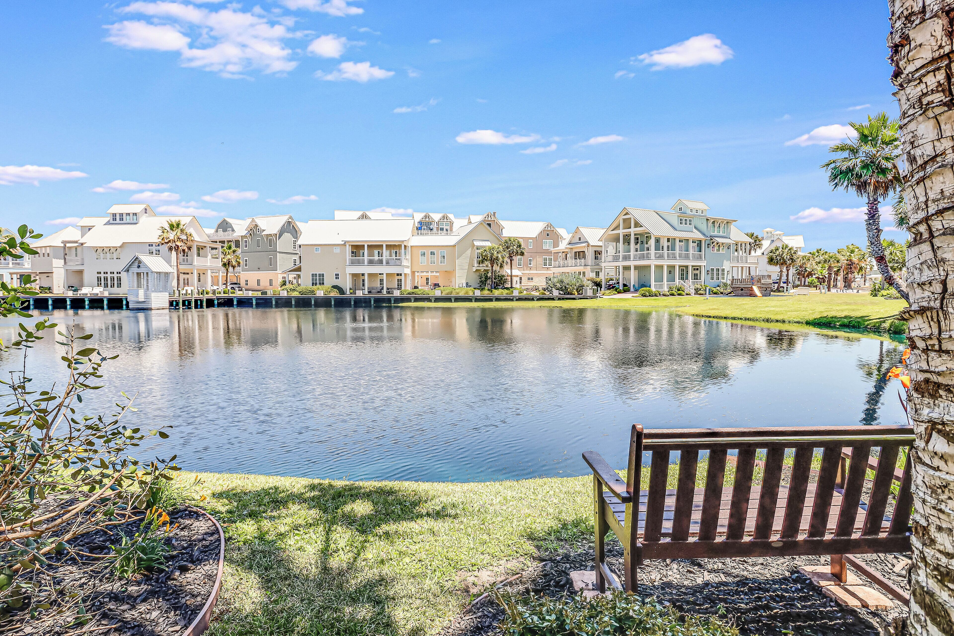 A waterfront view with a bench, a calm lake, and a row of multi-story buildings with balconies.