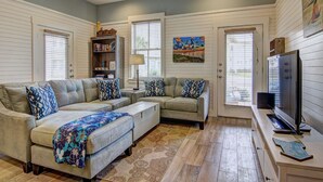 A living room with a sectional sofa, a television, and a bookshelf. - Watercolor Bungalow TC 2101 (Port Aransas)