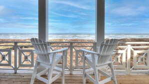 A covered deck with two white Adirondack chairs facing a beach view.