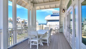 A covered outdoor deck with a white table and chairs, overlooking a beachfront property. - The Salty Dog 314 GR (Port Aransas)