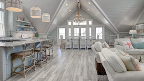A spacious loft with a high ceiling, a kitchen with a bar area, and a cozy seating area with a large window providing natural light. - The Salty Dog 314 GR (Port Aransas)