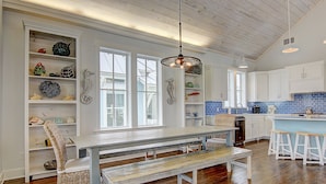A spacious kitchen with white cabinetry, a wooden bench, and a hanging light fixture. - Suits Us 231 BE (Port Aransas)
