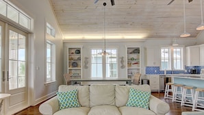 A spacious living room with a white sofa, a coffee table, and a kitchen area with white cabinets and blue tiles. - Suits Us 231 BE (Port Aransas)