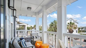 Un porche cubierto con mobiliario exterior, ventanas grandes y vistas a un barrio residencial.