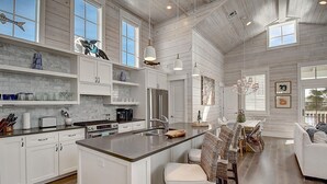 A spacious kitchen with white cabinetry, a central island, and a dining area with wicker chairs. - Sea Ya' Soon 130 ST (Port Aransas)