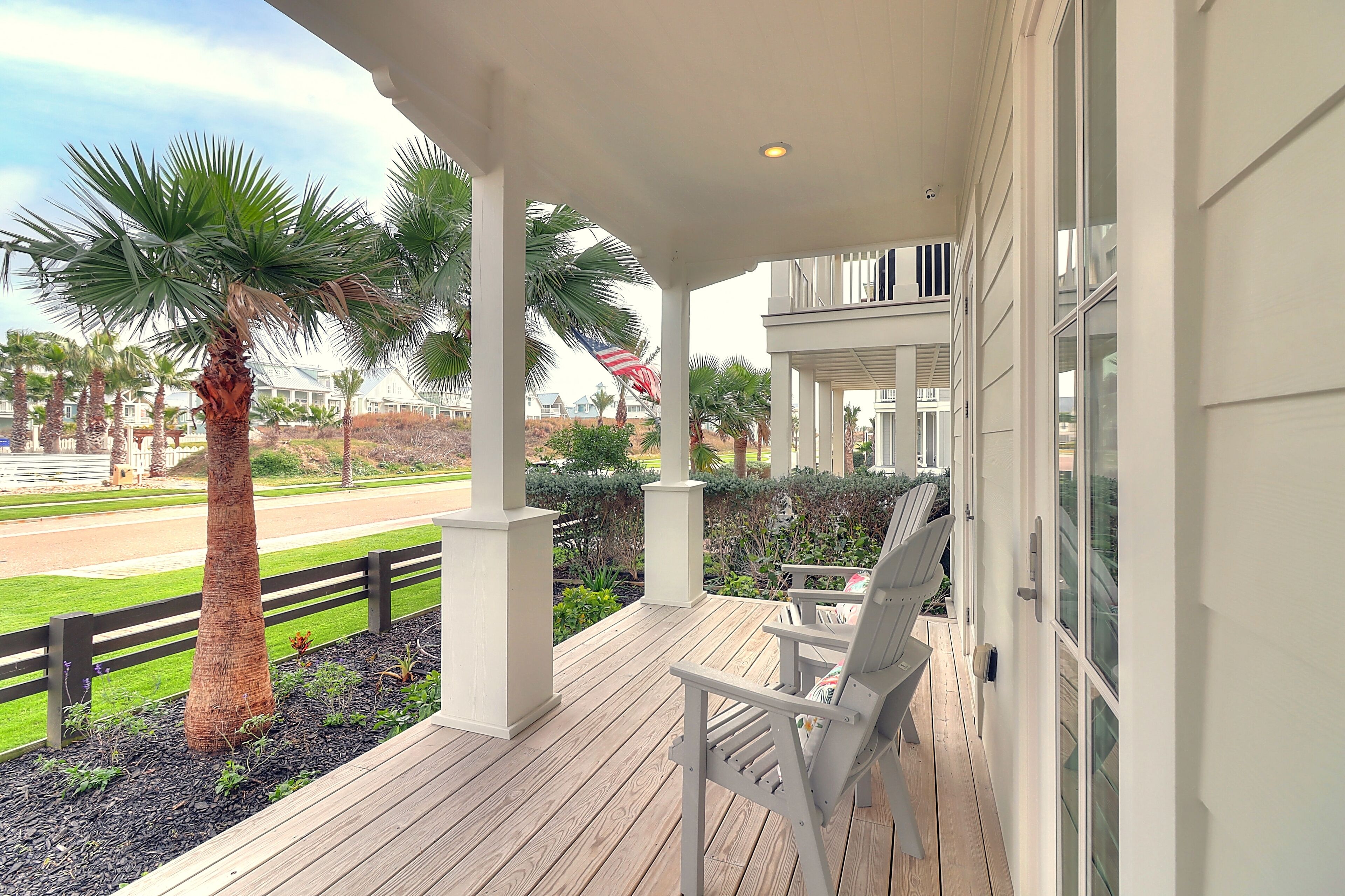 A covered outdoor area with a wooden deck, white columns, and two white chairs.