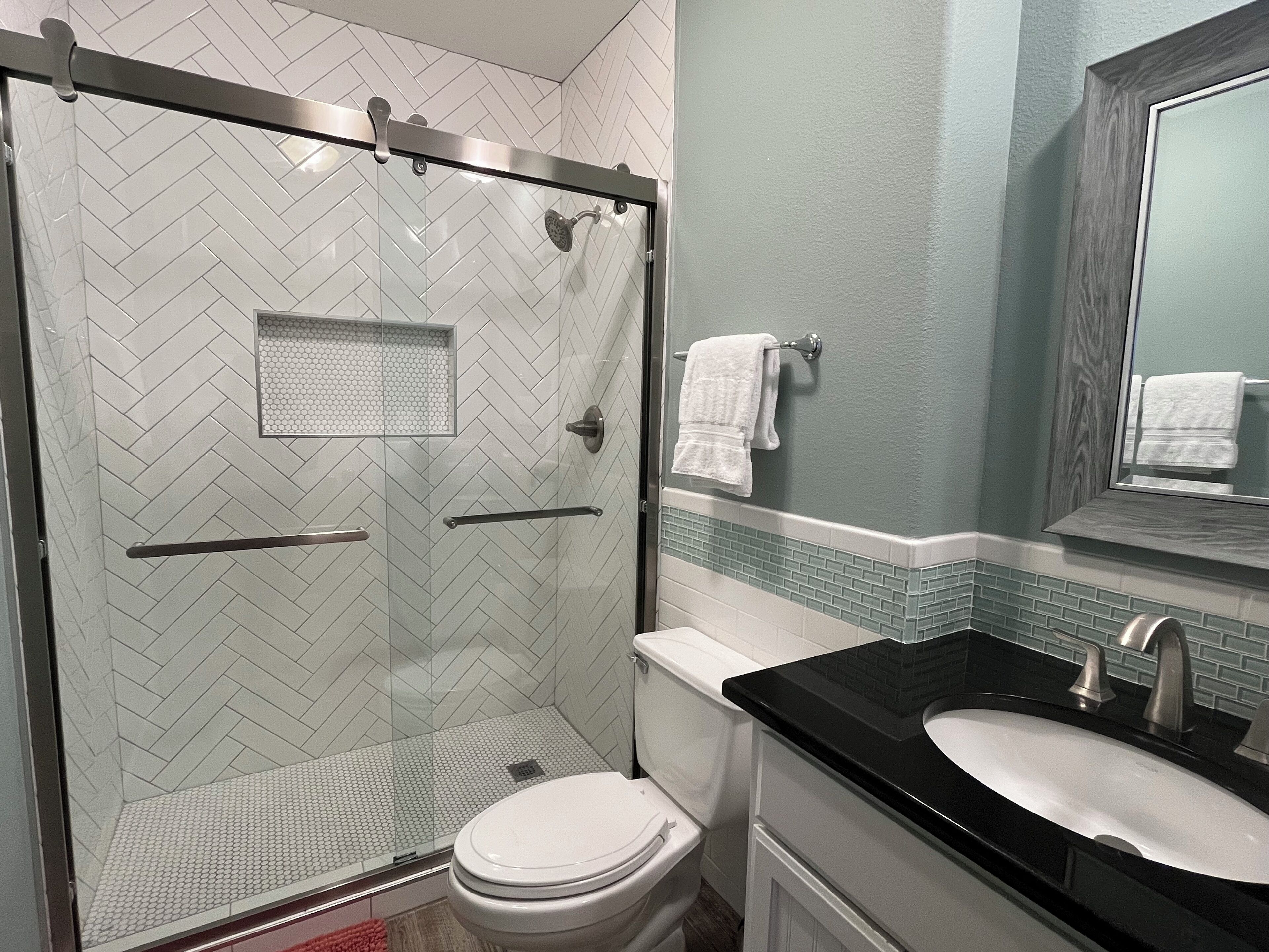 A bathroom with a glass shower enclosure, a white toilet, a black sink, and a mirror above the sink.