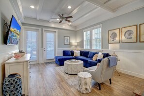 A spacious living room with a blue sectional sofa, a ceiling fan, and a large TV on the wall. - Sandy Toes TC 1102 (Port Aransas)
