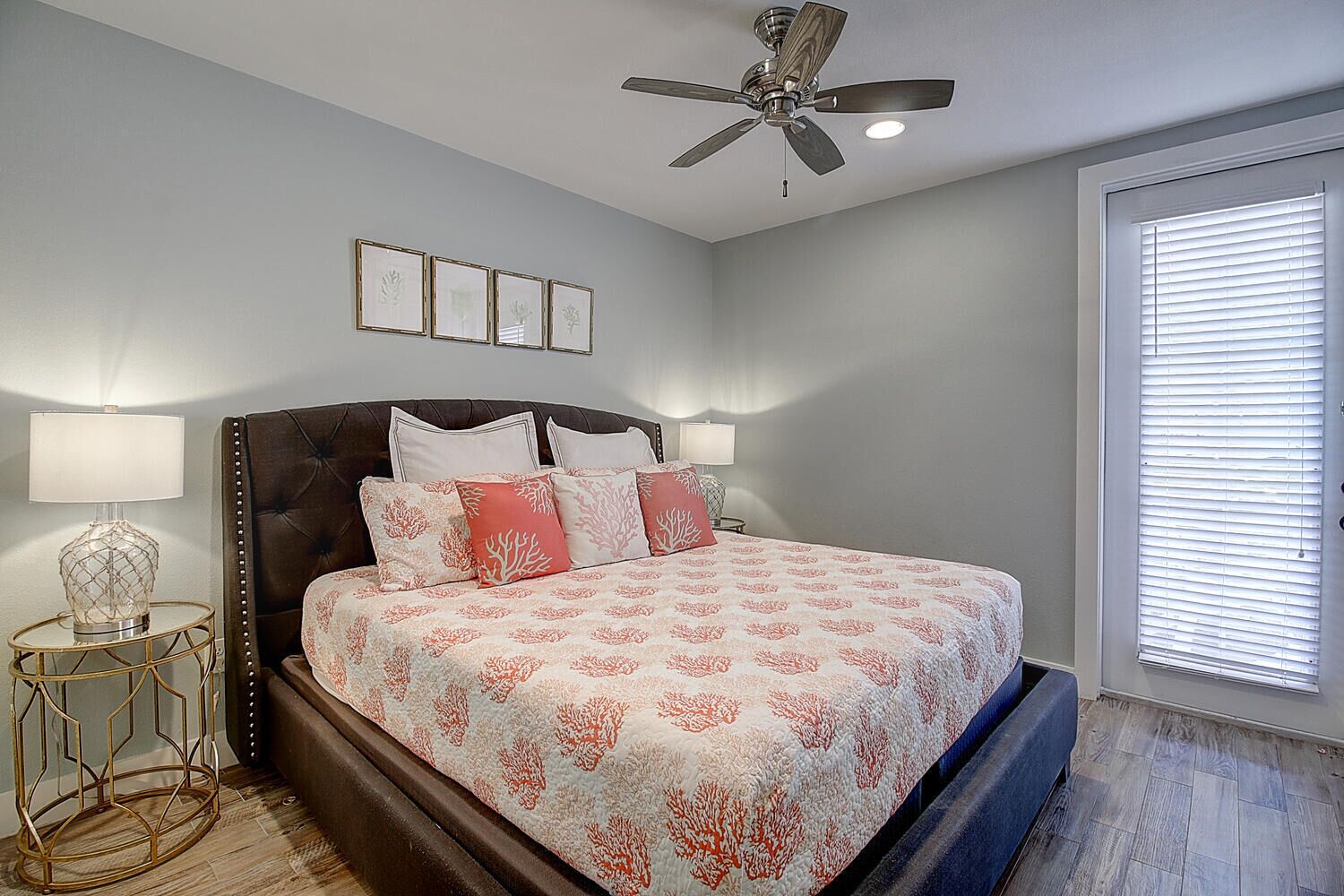 A bedroom with a bed, two bedside lamps, a ceiling fan, and a window with blinds.