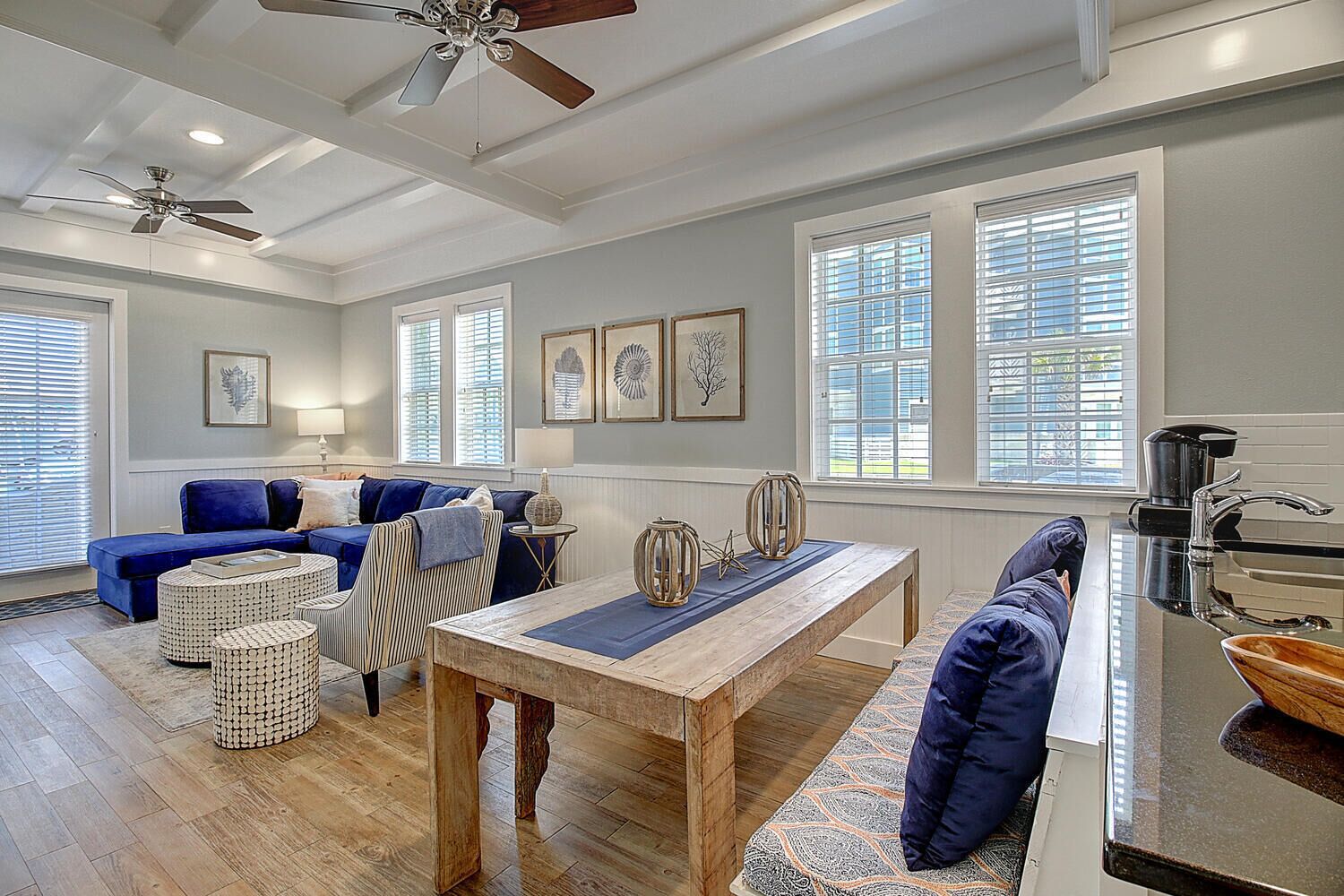 A modern living room with a blue sofa, wooden coffee table, and a dining area with a kitchen counter.