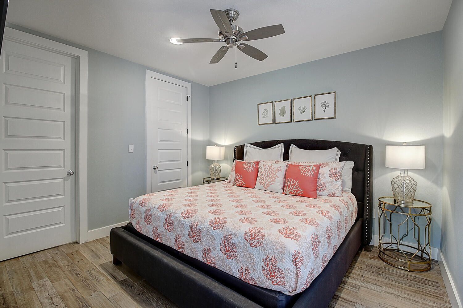 A bedroom with a bed, two bedside tables, a ceiling fan, and framed pictures on the wall.