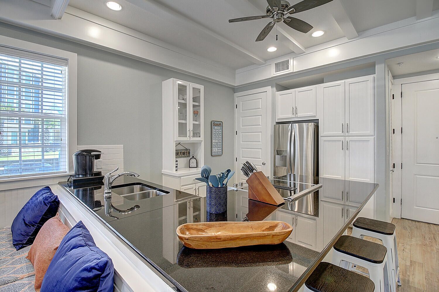 A modern kitchen with white cabinets, a stainless steel refrigerator, and a glass island with a wooden bowl.