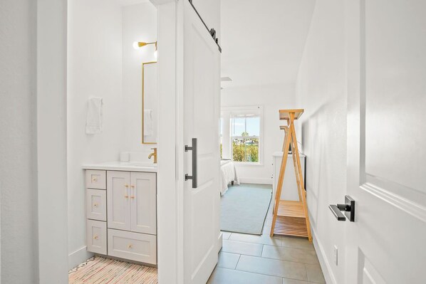Enter a serene space with a comfortable bedroom, featuring a large window, a vanity with mirror, and a convenient shelf.