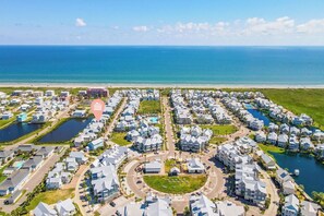 A coastal residential area with houses arranged in a grid pattern, a central circular park, and a beach in the background. - The Hideaway 249 HI (Port Aransas)