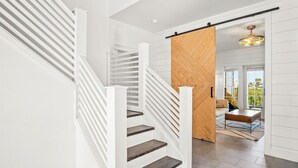 A modern staircase with white railings and dark steps, leading to a room with a wooden partition and a view of the outdoors. - The Hideaway 249 HI (Port Aransas)