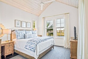 A bedroom with a bed, a nightstand, a lamp, framed pictures, a window with curtains, and a view of greenery outside. - The Hideaway 249 HI (Port Aransas)