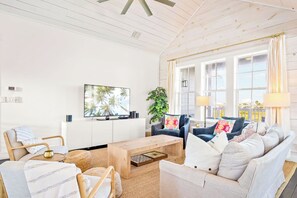 A spacious living room with a wooden ceiling, a large flat-screen TV mounted on the wall, a coffee table, and comfortable seating including a sofa and chairs. - The Hideaway 249 HI (Port Aransas)