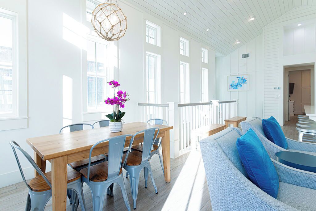 A bright, spacious room with a wooden dining table and chairs, a blue sofa, and a hanging light fixture.
