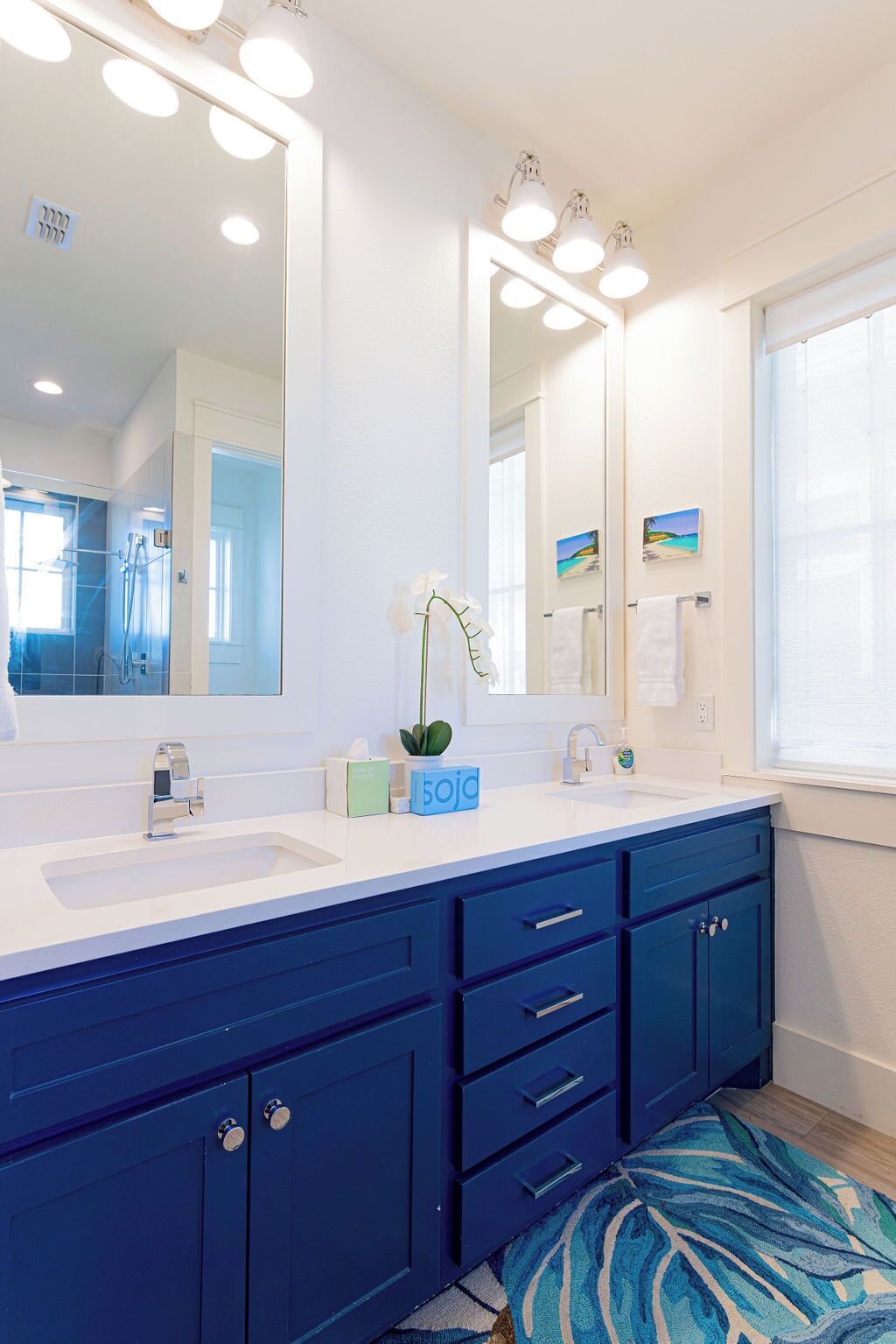 A modern bathroom with two sinks, a large mirror, and a blue cabinet.